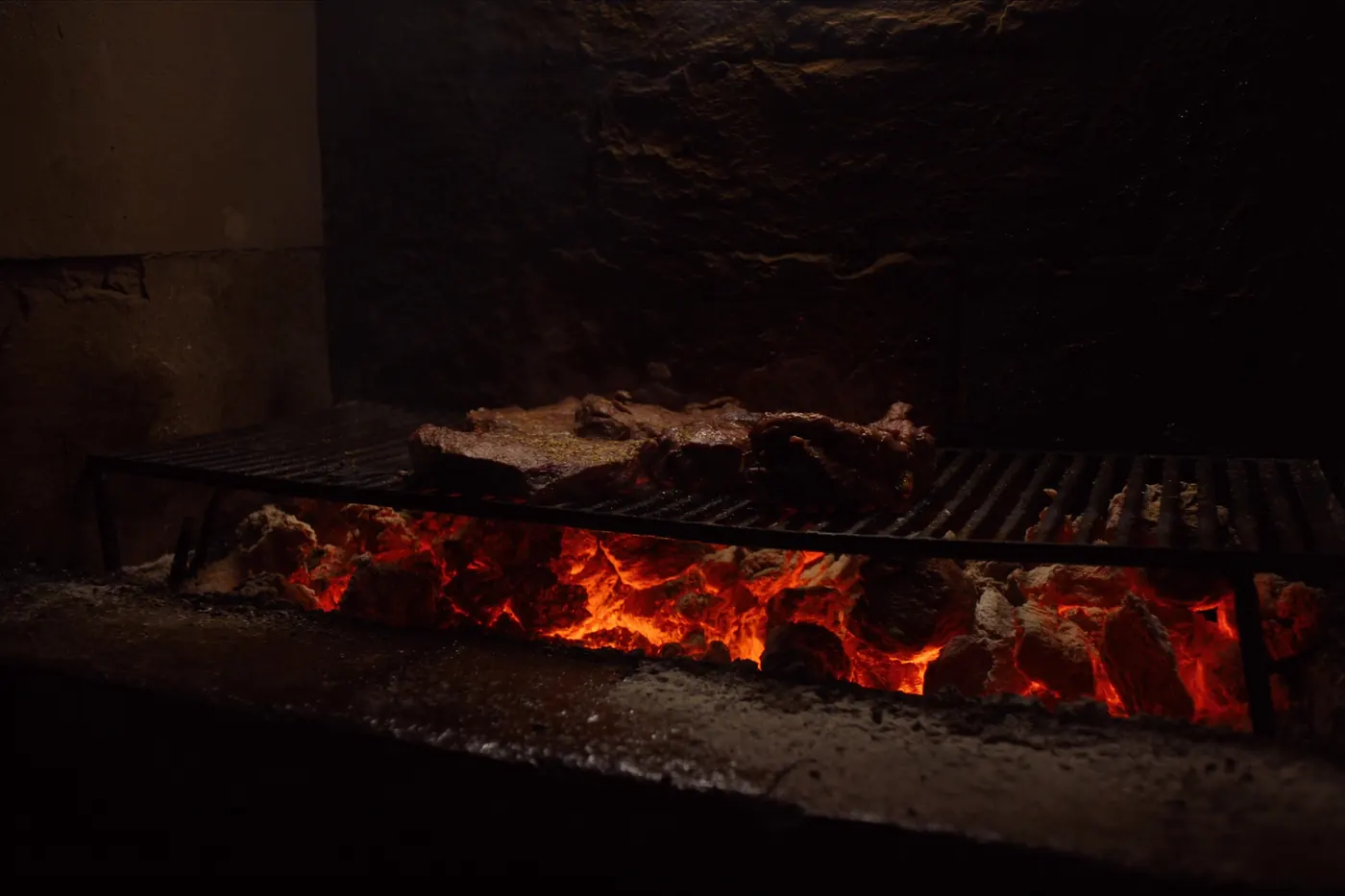 Beef searing over glowing charcoal on an open stone hearth