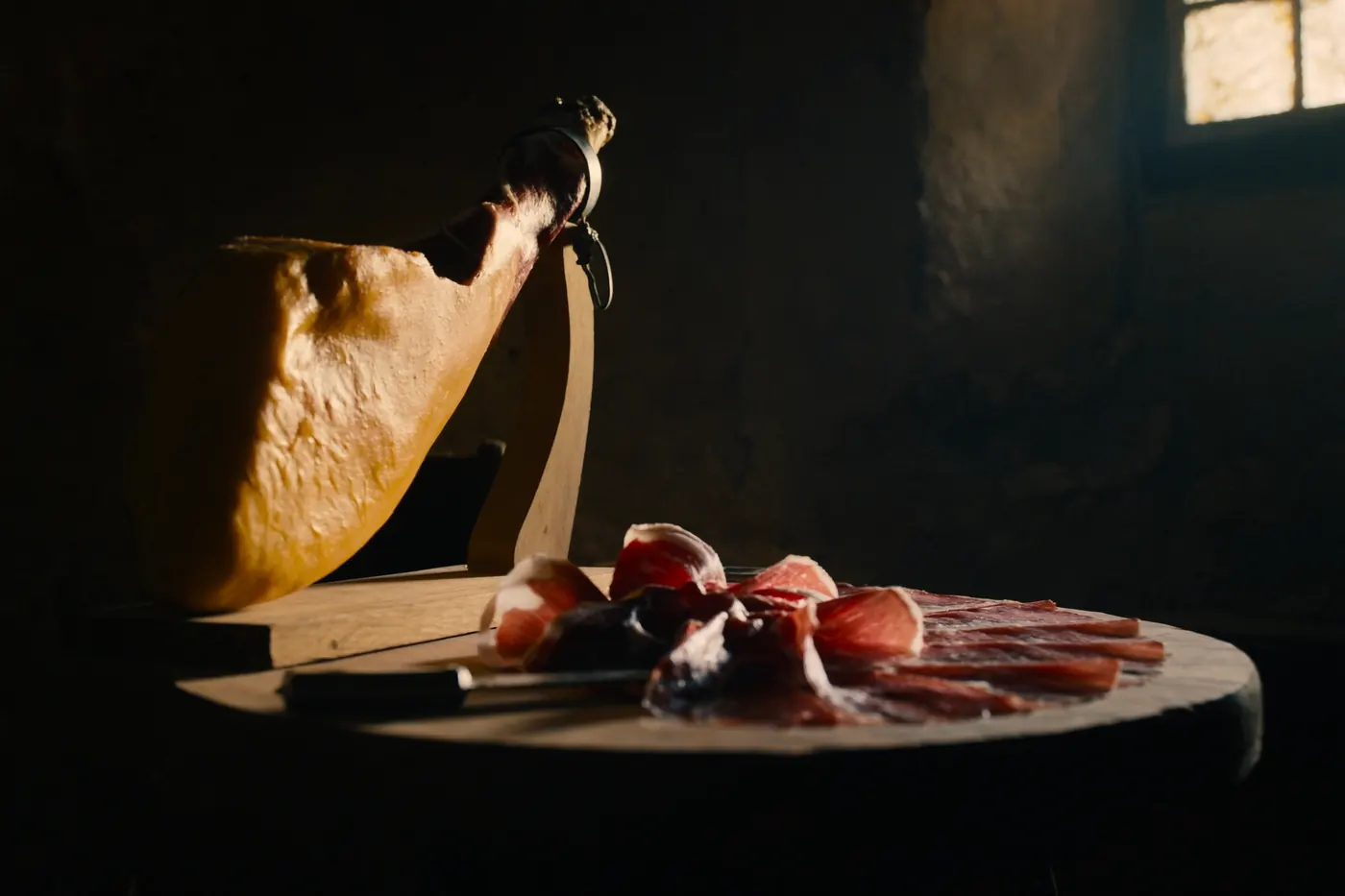 A whole leg of house-cured Istrian prosciutto with thin slices on a wooden board